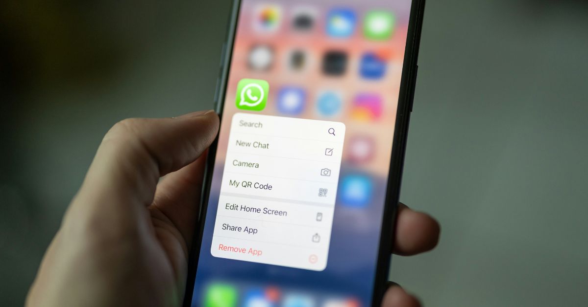 Person holding an iPhone with WhatsApp icon selected, showing app options including remove and share